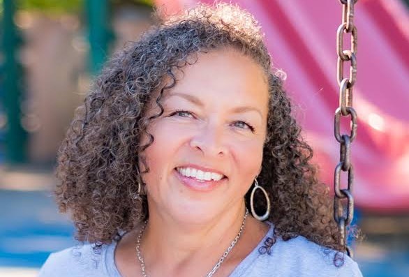 Middle-aged woman with curly medium-brown hair and a light blue shirt.