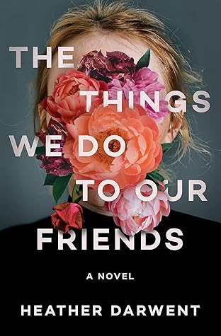 White woman with blond hair, black turtleneck, and pink flowers covering her face