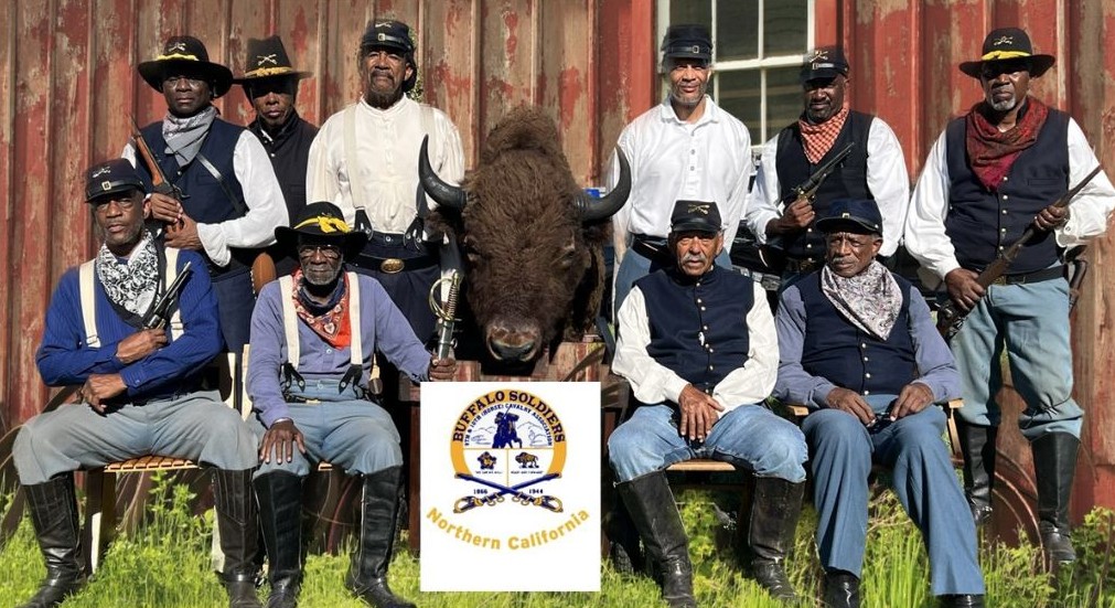 Group of ten older African American men dressed in Civil War soldier's uniforms sitting around a buffalo