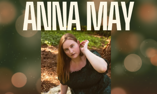 Anna May. Photo of young white woman with reddish blonde hair in a black shortsleeved dress pushing her hair behind her left ear.